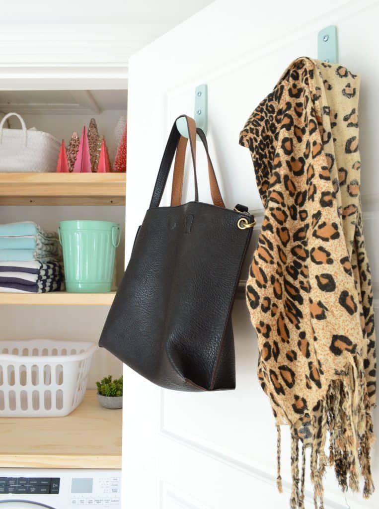 Laundry closet door with large colorful hooks with DIY laundry shelves in background