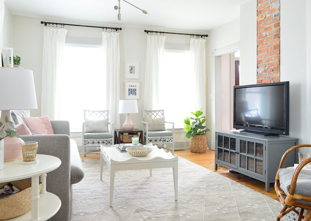 Beach house living room with exposed brick fireplace and two windows with floor to ceiling white curtains